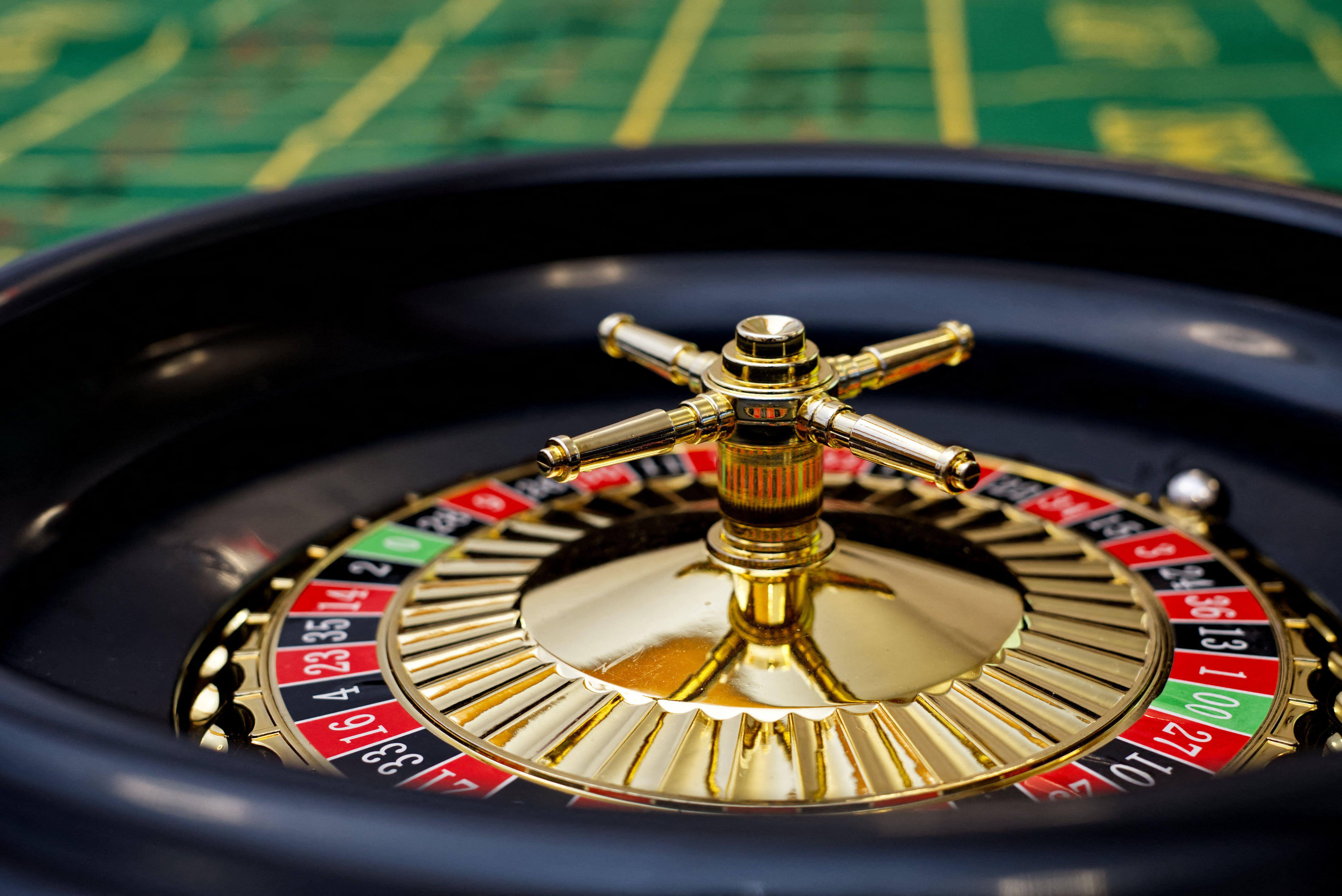 Close-up of a casino roulette wheel with gold spindle, red and black numbered slots, and a white ball, set on a green felt gaming table